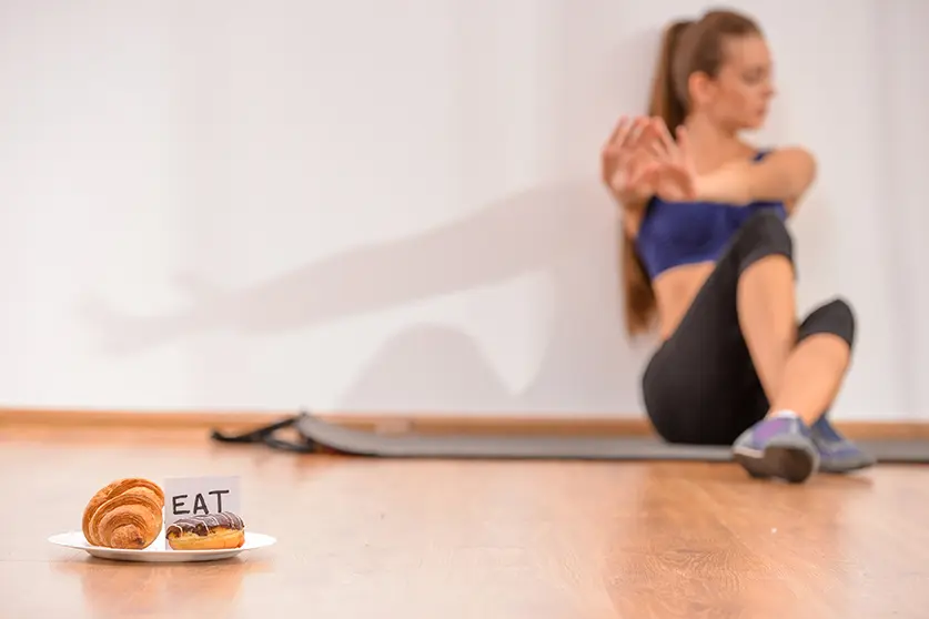 Young sadness woman is sitting on the floor. Focus on sweets. Concept of diet.