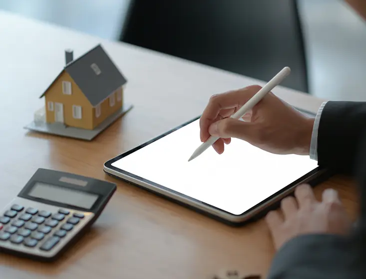 Close-up shot of Businesspeople use a pen to write on a tablet with model house and a calculator on the table.