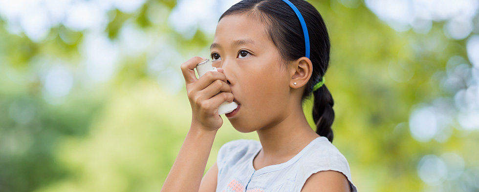 Girl using an asthma inhaler in the park