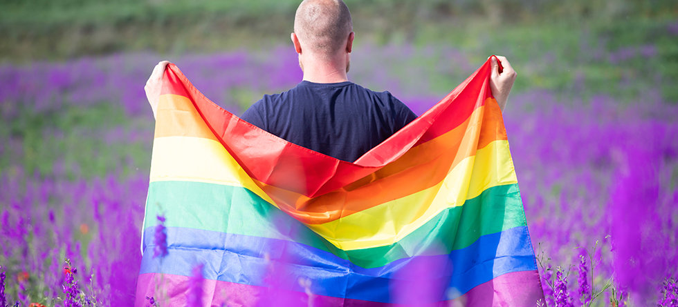 Man holding a Gay Rainbow Flag in beautiful summer field. Bisexual,gay, lesbian, transsexual symbol. Happiness, freedom and love concept for same sex couples
