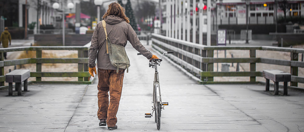 a single man dressed in old clothes on the embankment with the bike