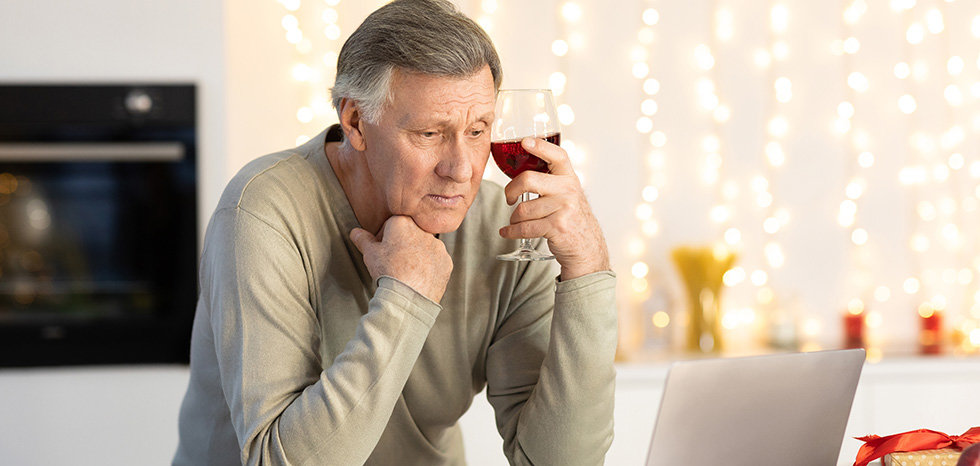 Lonely Elderly Man Celebrating Christmas Alone At Laptop Making Video Call To Distant Friend Sitting And Drinking Wine During Xmas Eve At Home. New Year Holiday Celebration During Covid-19 Quarantine