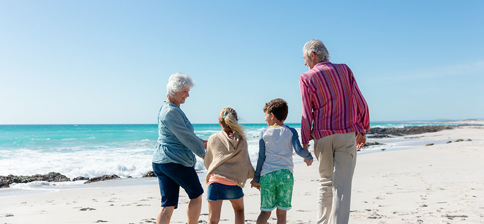 Rear view of a multi-generation Caucasian family on the beach with blue sky and sea in the background, walking and holding hands